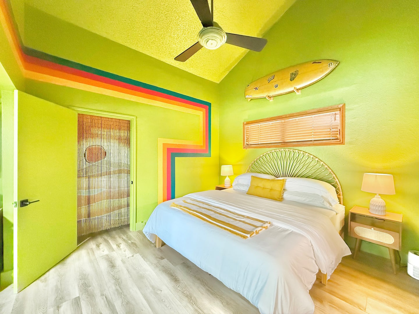 Bedroom 1 with a king bed, rainbow wall stripes and a surfboard on the wall
